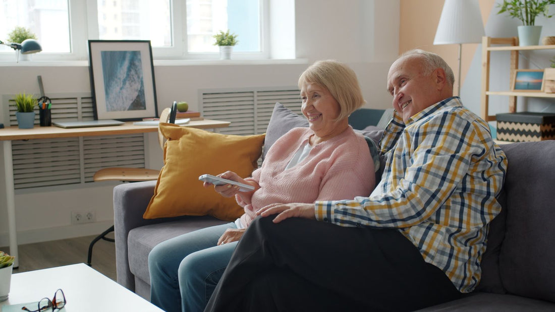 Un couple de seniors souriant regarde la télévision sur le canapé